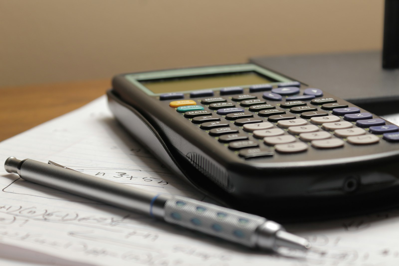 Une calculatrice posée sur des feuilles de calcul, à côté d'un stylo