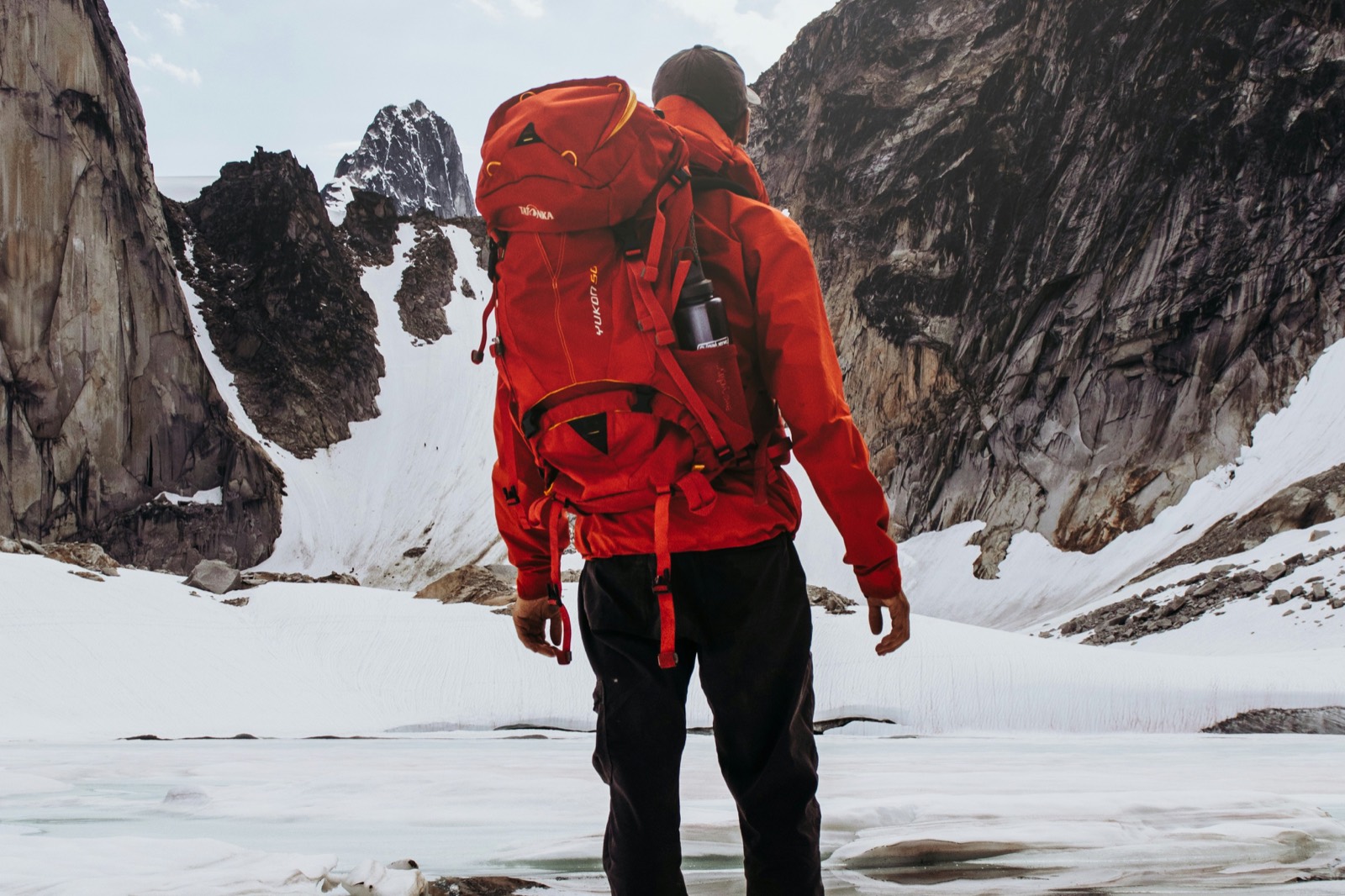Un randonneur sac au dos face à un cirque de montagnes enneigées